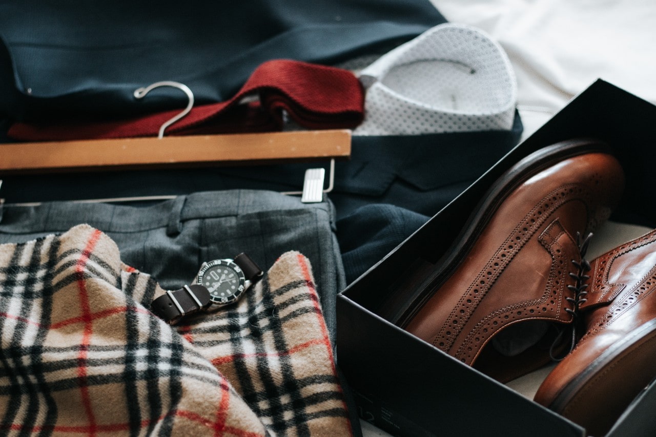 Suit, pants, scarf, watch, and dress shoes displayed on a bed, ready for someone to put on