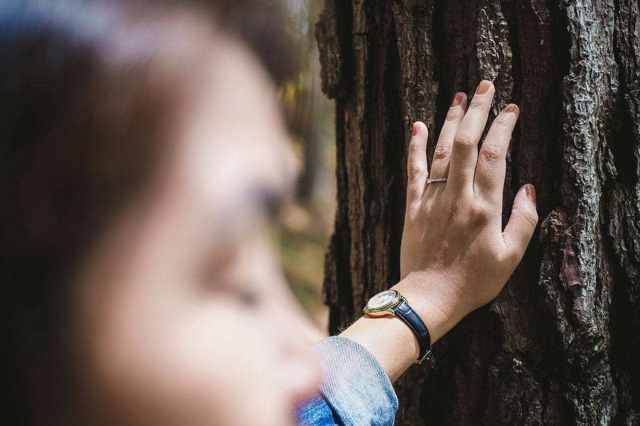 Fashionable lady holding her hand against a tree. She is considering taking her engagement ring off but decides against it