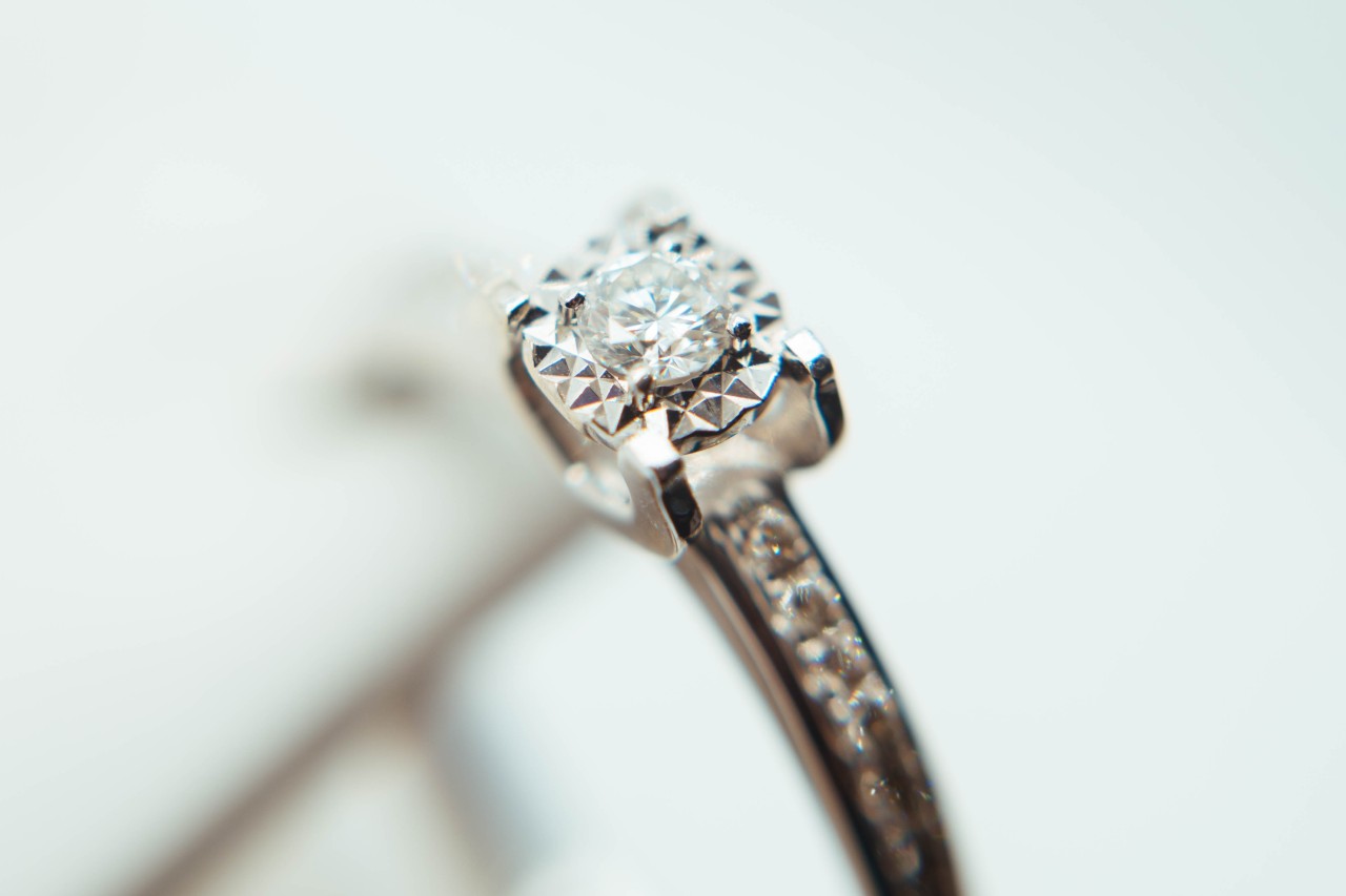 An engagement ring held close to the camera, the diamond shining bright in the foreground