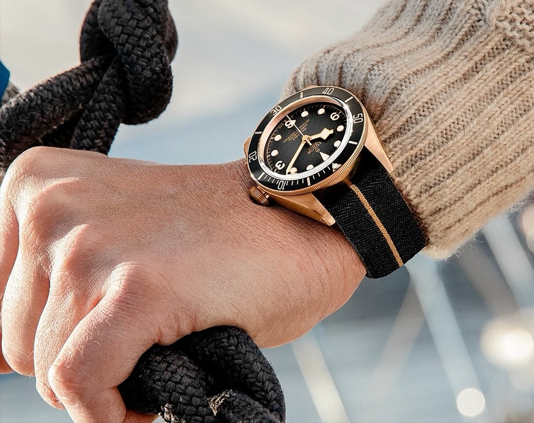 A close-up of a man’s wrist as he holds knotted rope, a luxury watch on his wrist.