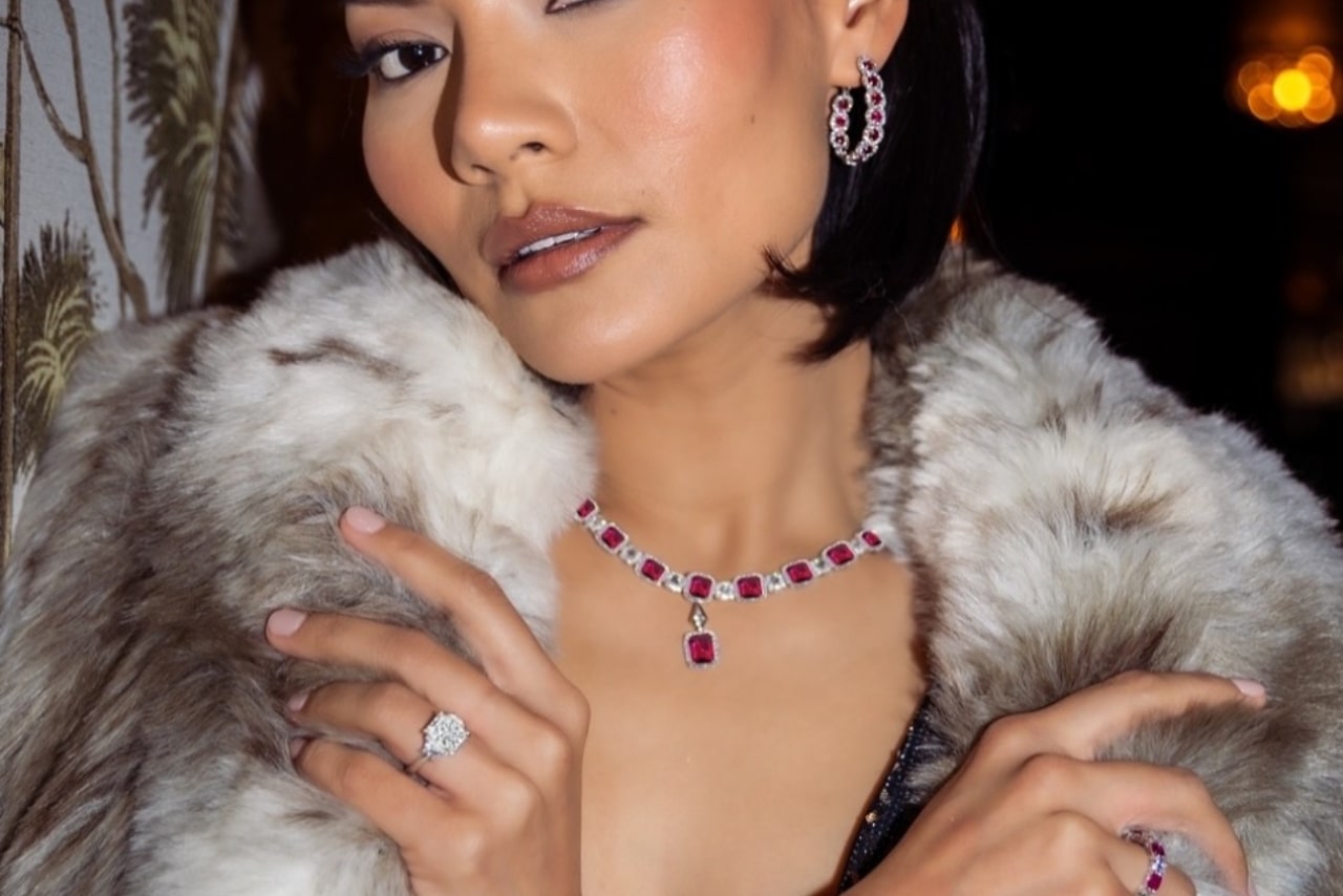 A glamorous woman wearing a set of ruby and diamond earrings, necklace, and ring, along with a beautiful diamond engagement ring