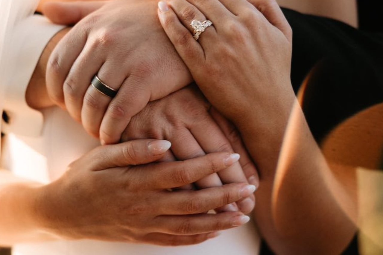 A couple embracing with a focus on her marquise center stone side stone engagement ring set in yellow gold