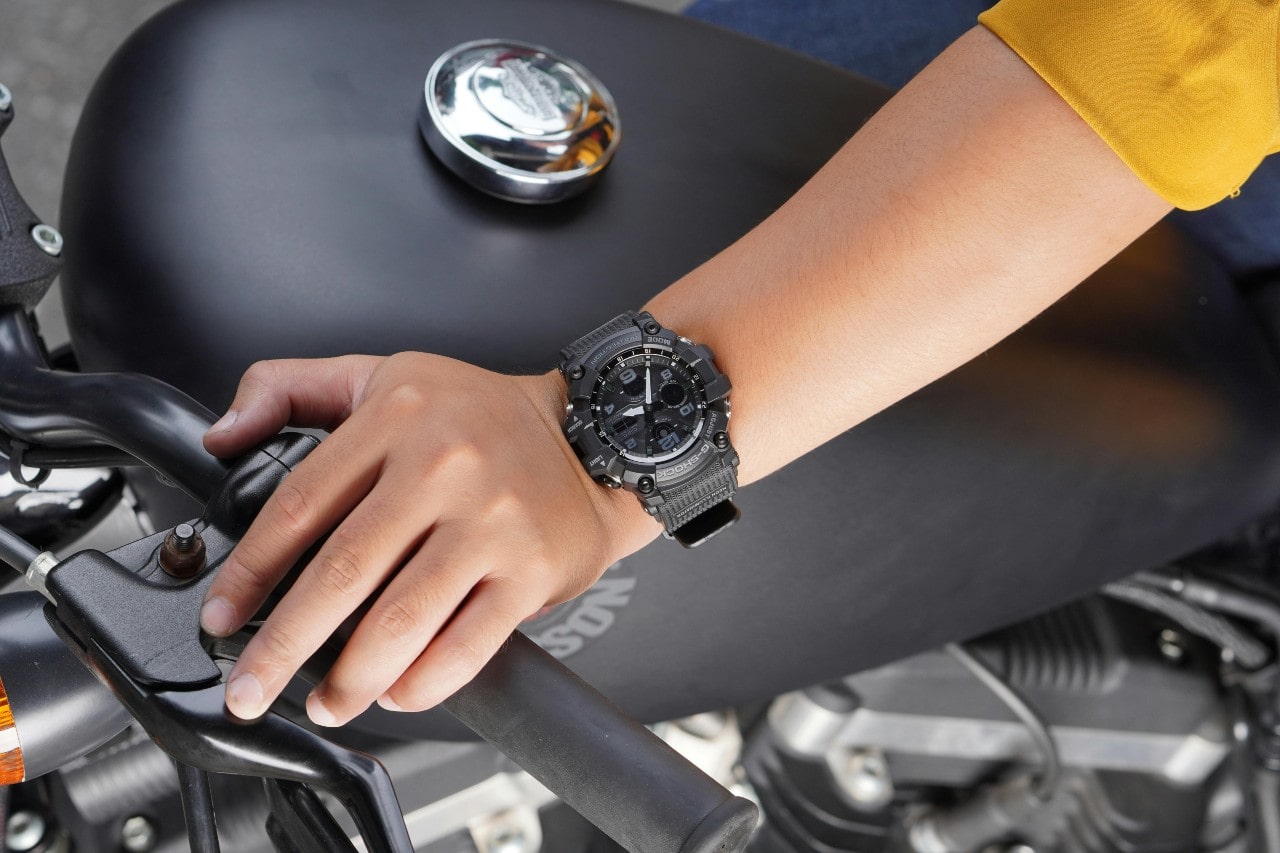 a person’s hand resting on a motorcycle handlebar, wearing a black G-Shock watch