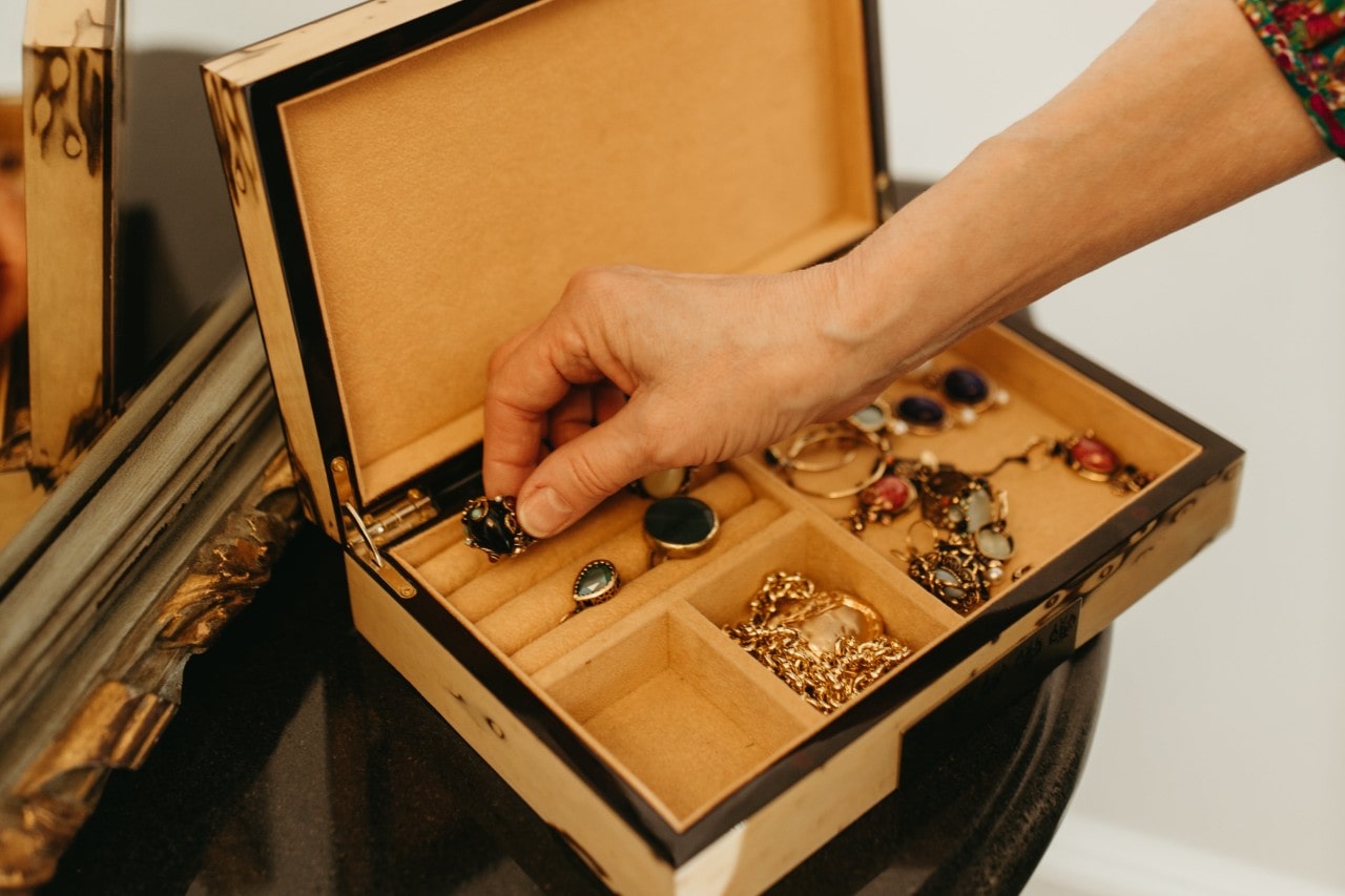 a hand placing a piece of jewelry inside a wooden jewelry box