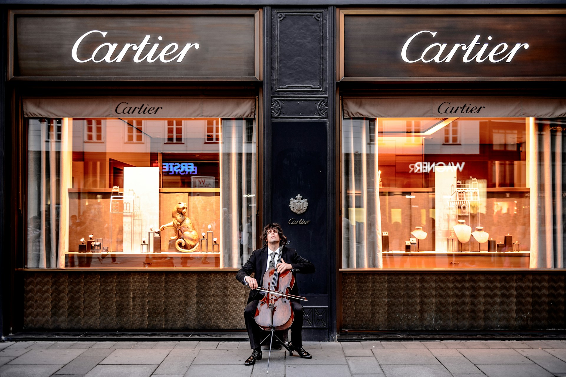 a man playing the cello sitting outside a Cartier store